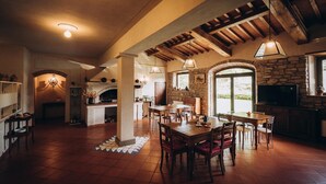 A spacious kitchen with a stone wall, wooden beams, and a large dining area with multiple tables and chairs.