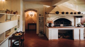 A kitchen with a brick fireplace, shelves with pottery, and a dining area with a table set for two.