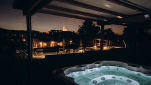 A hot tub under a covered area with a view of a lit-up building in the background.