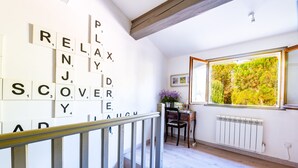 A staircase with a wooden handrail leading to a room with a white radiator, a window with a view of greenery, and a wall with Scrabble tiles spelling out words. - Villa Nyons Drôme provençale private heated pool Wifi Bbq (Nyons)