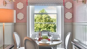 En matplats med ett bord dukat för två personer, ett fönster med utsikt över grönskan och tapeter med ett mönster.