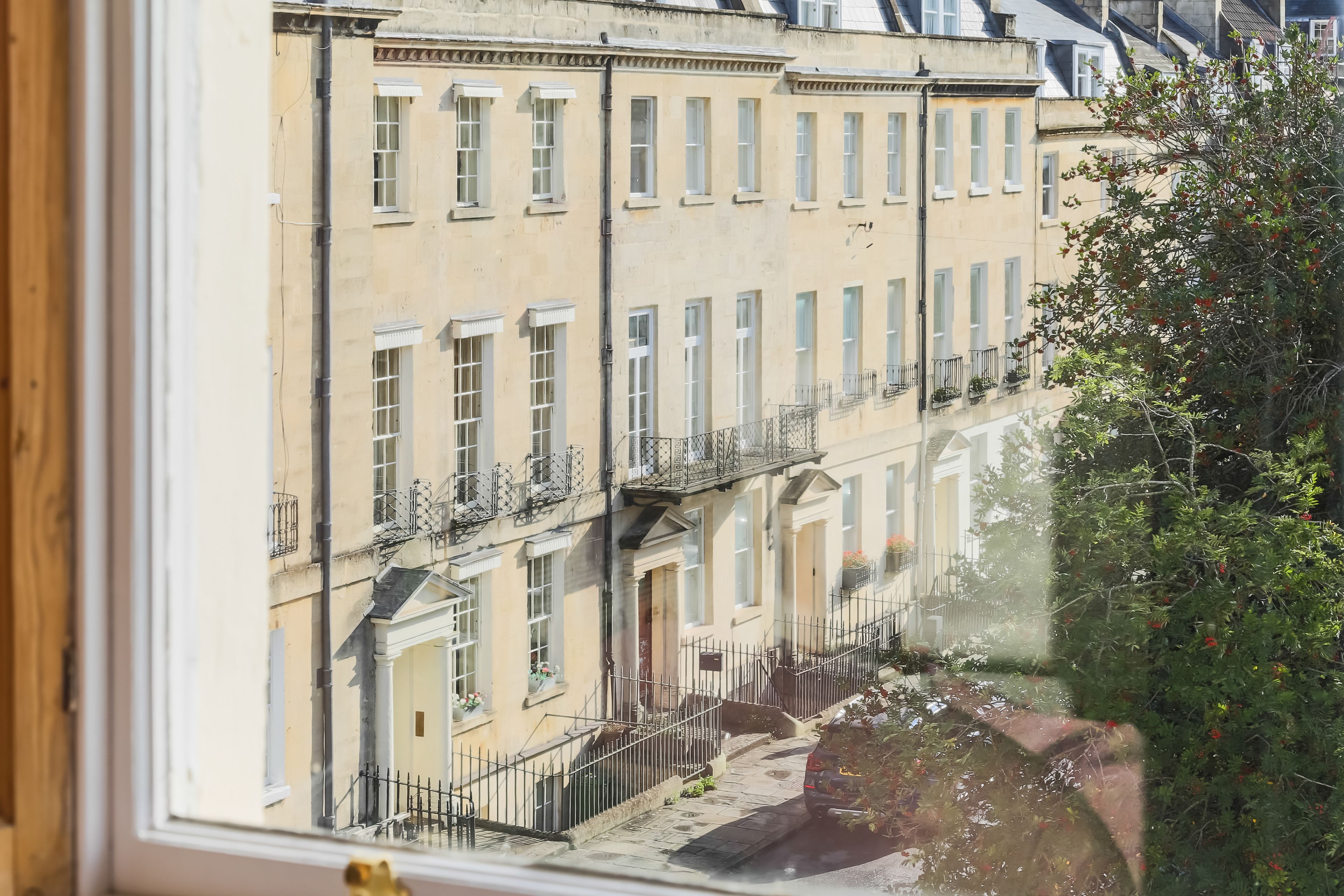 Une rangée de bâtiments aux fenêtres et balcons uniformes, un ciel dégagé et un arbre au premier plan.