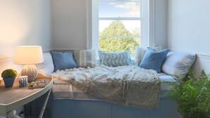En mysig hörna med en soffa, en lampa, ett litet bord med en växt och utsikt över grönskan utanför.