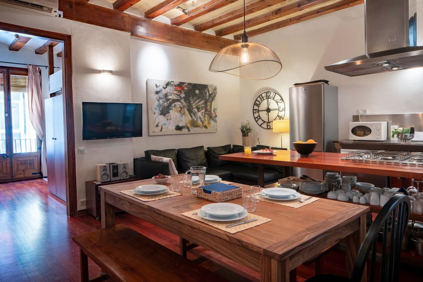 A modern kitchen with wooden flooring, a dining table set for four, a large clock, and a microwave.