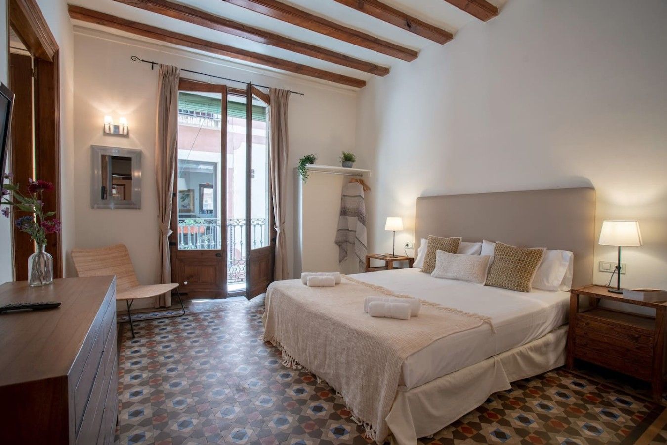 A bedroom with a large bed, bedside tables, a chair, a desk, and a patterned floor.