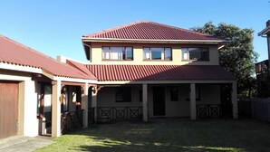 A two-story building with a red roof and beige walls, featuring a covered patio area with a railing.