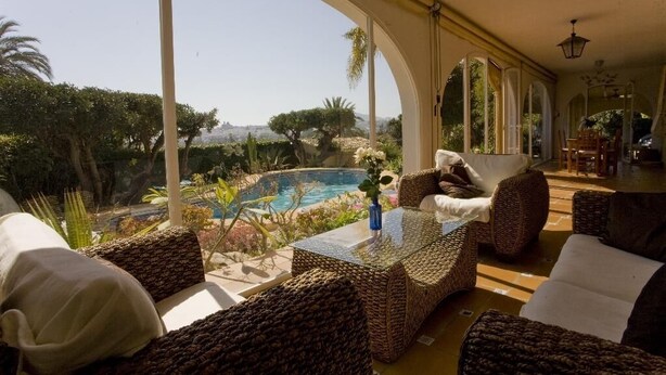 A sunlit room with wicker furniture, a glass table, and a view of a swimming pool and garden. - Finca el Tossal, Altea (Altea)