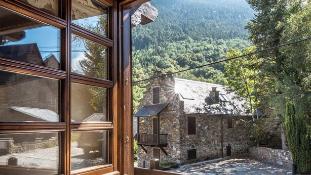 A stone building with a wooden balcony, a stone wall, and a view of a forested mountain. - Solei by FeelFree Rentals (Garòs)
