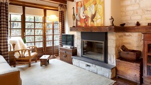 A cozy living room with a fireplace, wooden furniture, and a large window with curtains. - Solei by FeelFree Rentals (Garòs)