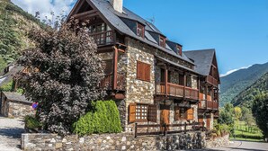 A stone building with multiple balconies and a steep roof, surrounded by lush greenery and mountains. - Solei by FeelFree Rentals (Garòs)