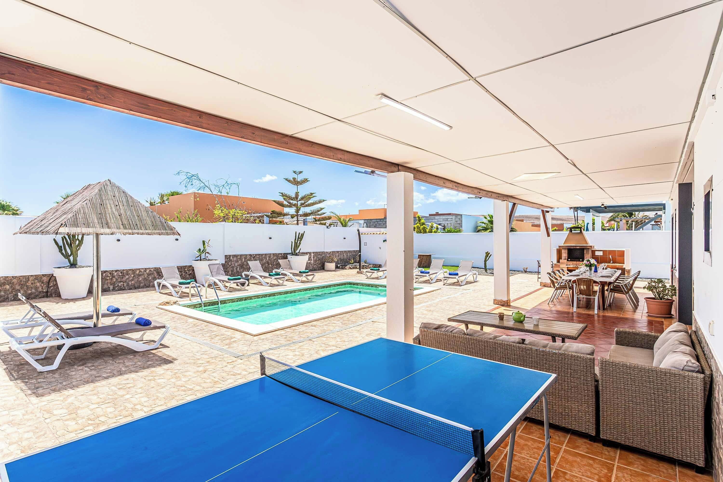 A pool area with a ping pong table, lounge chairs, and a barbecue area.