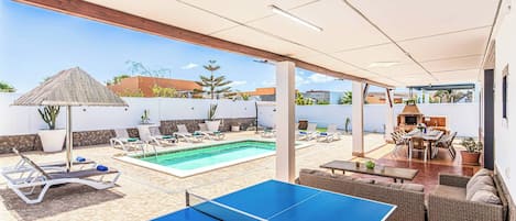 Área de piscina com mesa de tênis de mesa, espreguiçadeiras e espaço para churrasco.