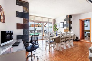 A modern dining area with a view of the outdoors, a dining table set with chairs, and a computer desk with a monitor and keyboard.