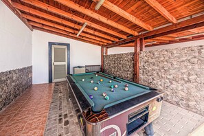 Ein Billardtisch im Freien mit einer Steinwand im Hintergrund und einer Holzbalkendecke.