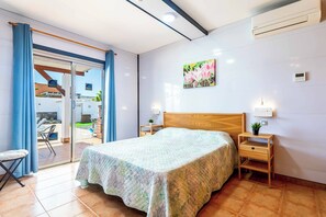 Ein Schlafzimmer mit einem Bett, einem Nachttisch, einer Wand-Klimaanlage und einer Glastür, die zu einem Außenbereich führt.