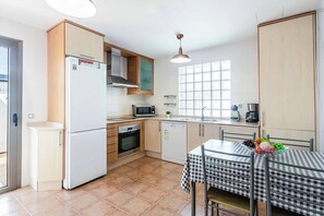 A compact kitchen with a refrigerator, microwave, oven, and dishwasher. There is a window providing natural light and a table with a checkered tablecloth. - Villa Susi - Five Bedroom Villa, Sleeps 10 (Fuerteventura)
