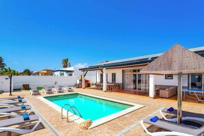 Ein Swimmingpool mit Liegestühlen, eine überdachte Terrasse und ein modernes Gebäude mit großen Fenstern.