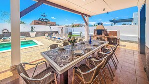 An outdoor dining area with a view of a swimming pool and a barbecue grill. - Villa Susi - Five Bedroom Villa, Sleeps 10 (Fuerteventura)