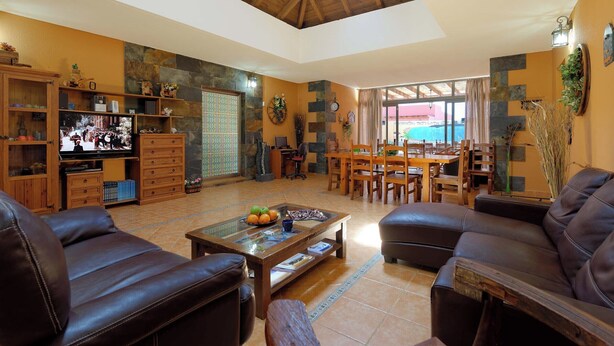 A spacious living area with a high ceiling, a television, a dining table with chairs, and a sofa.