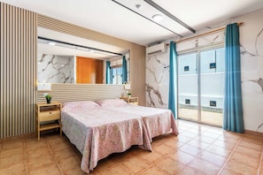 Ein Schlafzimmer mit Bett, Kommode, Spiegel und Meerblick durch eine Schiebetür.