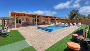 A pool area with a pergola, artificial grass, and outdoor seating.