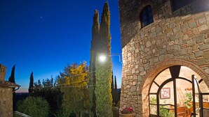 A stone building with a large arched doorway, a well-maintained garden, and a clear night sky. - Old Stone Apartment Perona (Cinigiano)