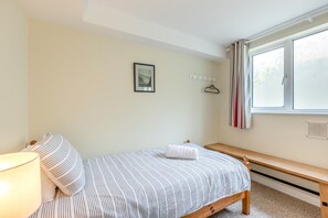 A bedroom with a bed, a bedside table, a lamp, a bench, a window with curtains, and a coat rack with hangers. - 3 Bed in Clifton Court (oc-fl8) (Croyde)