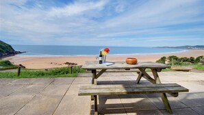A wooden picnic table with a bottle and flowers, overlooking a beach. - 3 Bed in Clifton Court (oc-fl8) (Croyde)