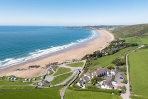 Luftaufnahme einer Küstenlandschaft mit Strand, Wohngebäuden und grünen Feldern.