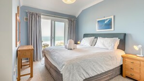 A bedroom with a bed, a nightstand, a wooden stool, a window with curtains, a ceiling light, and a framed picture on the wall. - 3 Bed in Clifton Court (oc-fl8) (Croyde)