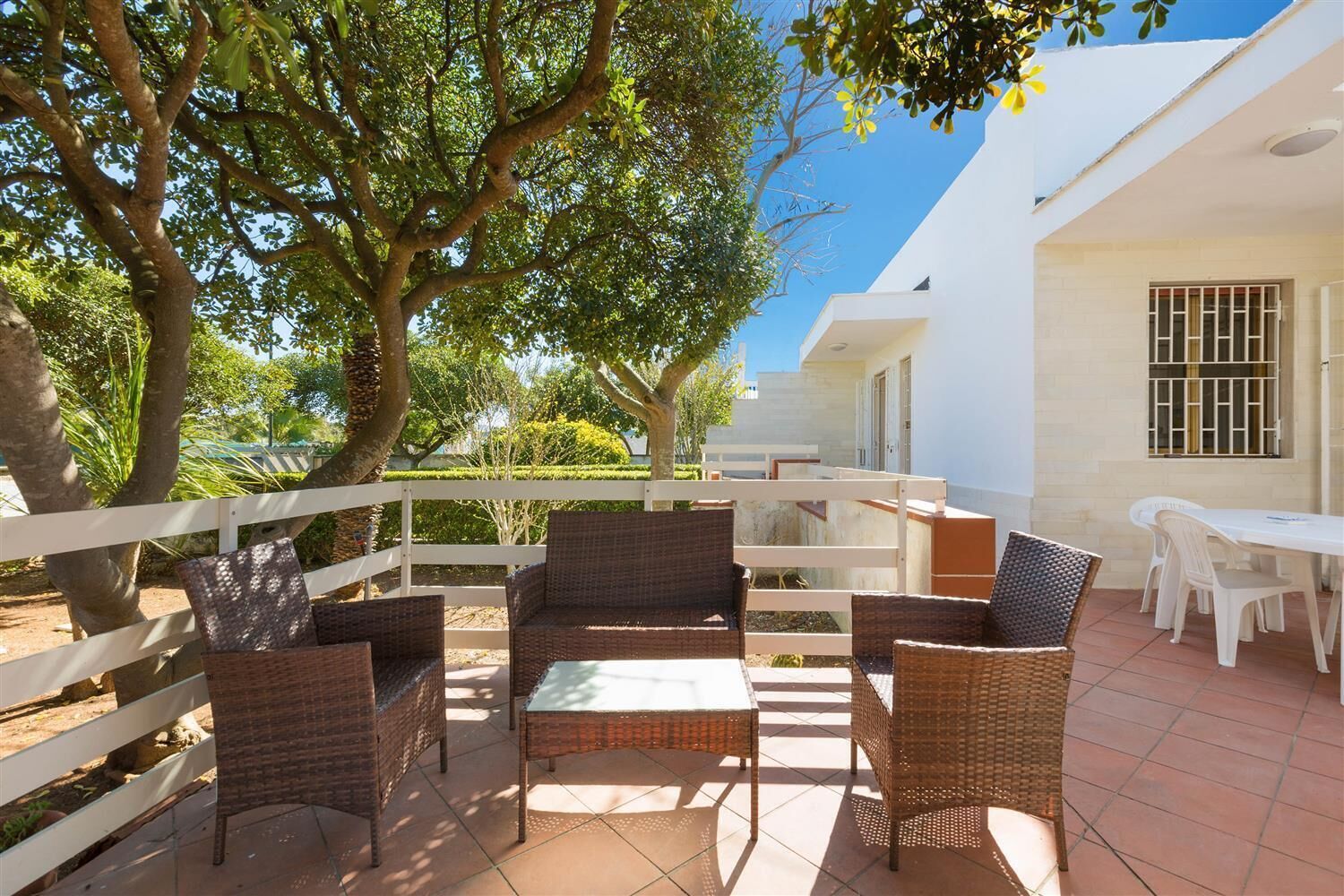 An outdoor patio area with wicker furniture and a white fence.