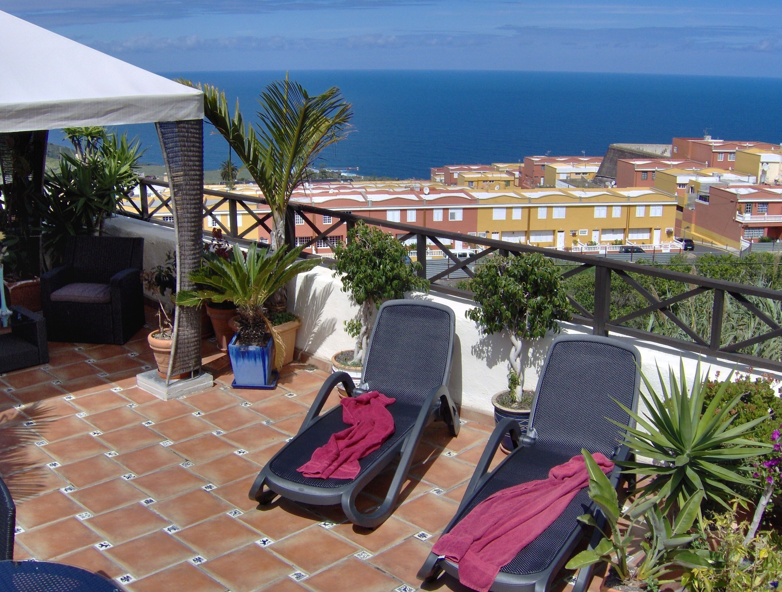 A terrace with two lounge chairs, a white umbrella, and potted plants.