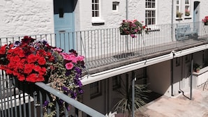 A white building with multiple windows and doors, a balcony with a railing, and flower baskets.