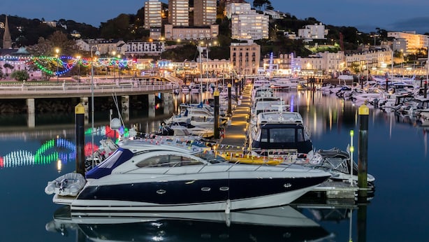 A marina with boats docked, a bridge, and buildings in the background.