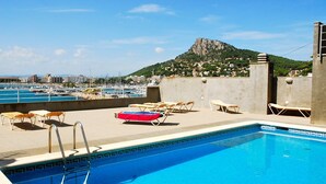 Una piscina en la azotea con sillones de descanso, vista hacia un puerto deportivo y una montaña al fondo.