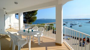 Un balcón con sillas y una mesa blancos, con vista a un puerto deportivo con barcos y una vista despejada del mar.
