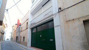 A narrow street with a building featuring a green garage door and a sign reading "LA TIMPAPA".