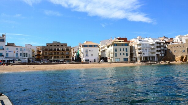 A coastal town with buildings along the beach, clear blue sky, and calm sea.