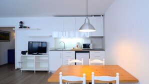 A compact kitchen with white cabinets, a wooden dining table, and a TV.