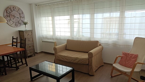 Un salon avec une table en bois, un canapé beige, une table basse en verre, une chaise en bois et une horloge au mur.
