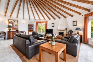 A living room with a fireplace, leather sofas, a wooden coffee table, and a large wooden ceiling beam.