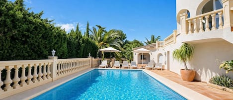 A swimming pool with a tiled edge, surrounded by a white building with arched windows and a balcony.