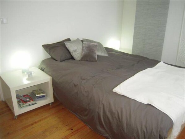 A bedroom with a bed, a nightstand with a lamp, and a magazine rack.