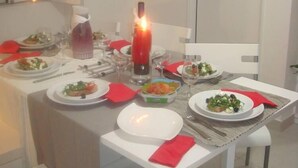 Un comedor con una mesa dispuesta para cuatro personas, con platos de comida, vasos y una vela.
