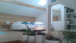 Un dormitorio con techo de madera, cama con ropa de cama blanca, tragaluz y una estantería.