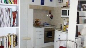 Una cocina compacta con armarios blancos, un microondas y un pequeño comedor con una silla roja.