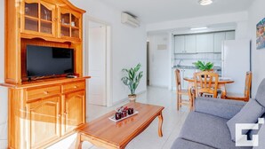 Una sala de estar moderna con un mueble de entretenimiento de madera, un televisor de pantalla plana, un sofá, una mesa de centro y un comedor con mesa y sillas.