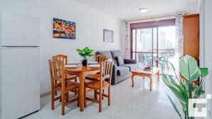 Una sala moderna con comedor, un sofá gris, una mesa de centro y un balcón con vistas a edificios.