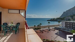 Un balcón con mesa y sillas, con vista a una playa y a un litoral montañoso.