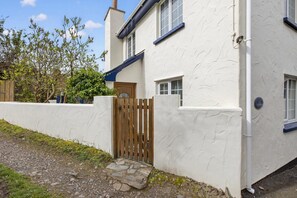 Un bâtiment blanc avec une porte en bois, un chemin de pierre et un ciel dégagé.